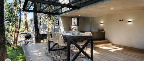 A modern outdoor dining area with a glass ceiling, a grill, and a dining table set for four.
