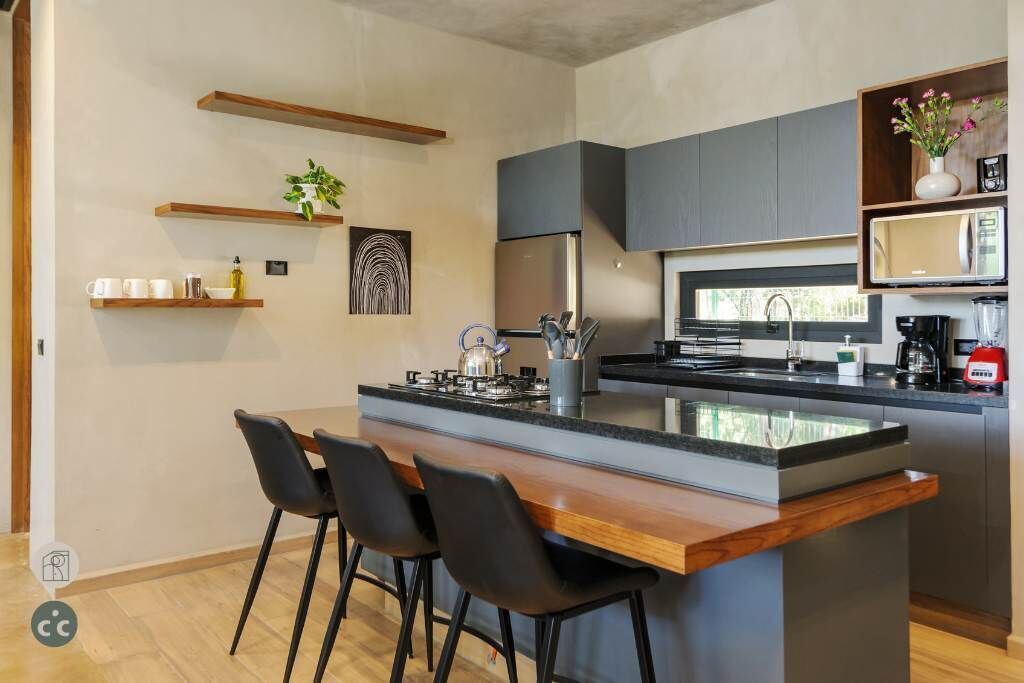 A modern kitchen with a central island, bar stools, a microwave, and a coffee machine.