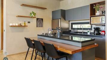 A modern kitchen with a central island, bar stools, a microwave, and a coffee machine.
