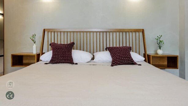Ein Bett mit Holz-Kopfteil, zwei Nachttische mit kleinen Topfpflanzen und zwei Wandleuchten.