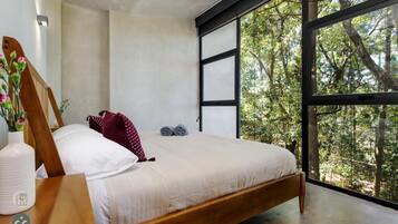 A modern bedroom with a large window, a wooden bed, and a white vase with flowers.