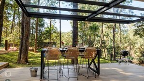 Ein Essbereich im Freien mit Glasveranda, umgeben von Bäumen.