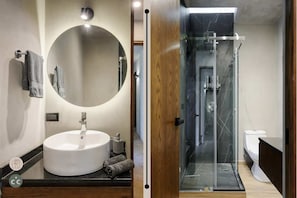 A modern bathroom with a round mirror, a white sink, and a glass-enclosed shower.