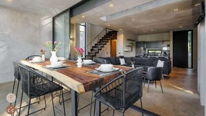 Una cocina moderna con una isla grande, una zona de comedor con una mesa de madera y sillas negras, y una escalera que sube a otro nivel.