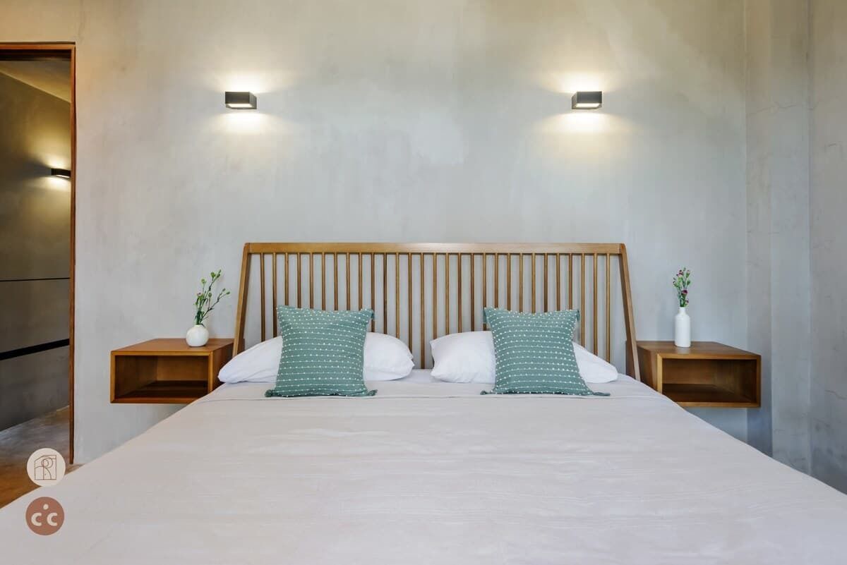 A modern bedroom with a large bed, two bedside tables with small plants, and a wooden headboard.