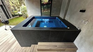 Un jacuzzi moderno al aire libre con terraza de madera y vista al jardín.