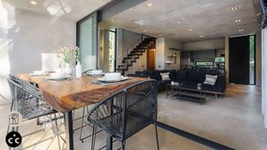 Un intérieur moderne comprenant un coin repas, des chaises noires, une table en bois et un escalier menant à un espace de vie avec un canapé noir.