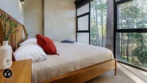 Une chambre moderne avec une grande fenêtre, un cadre de lit en bois et une table de chevet ornée d’un vase.