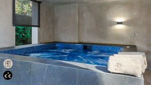 Un espace bien-être comprenant un jacuzzi, des murs carrelés et une fenêtre donnant sur un paysage verdoyant.