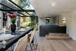 Un espace de restauration extérieur moderne, doté d’une structure vitrée, d’une table noire, de chaises blanches et d’un vase rempli de fleurs.