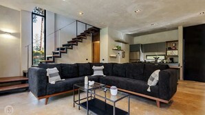 Ein modernes Wohnzimmer mit einem Ecksofa, einem Glastisch und einer Treppe, die in eine obere Etage führt.