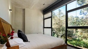 Ein Schlafzimmer mit großem Fenster, einem Holzbett und Blick auf Bäume.