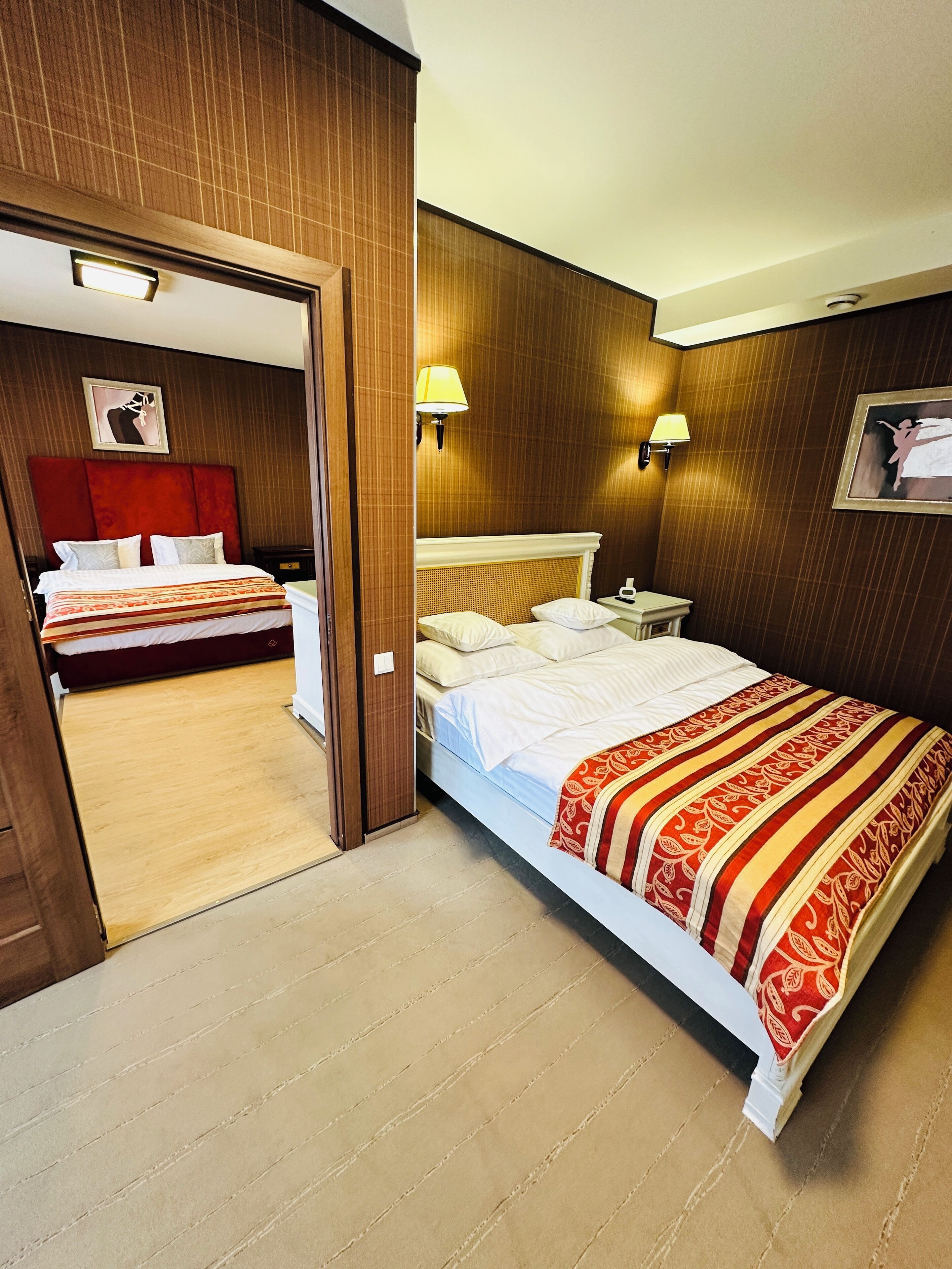 Ein Hotelzimmer mit zwei Betten, Holzvertäfelung, einem roten Kopfteil und zwei Wandlampen.