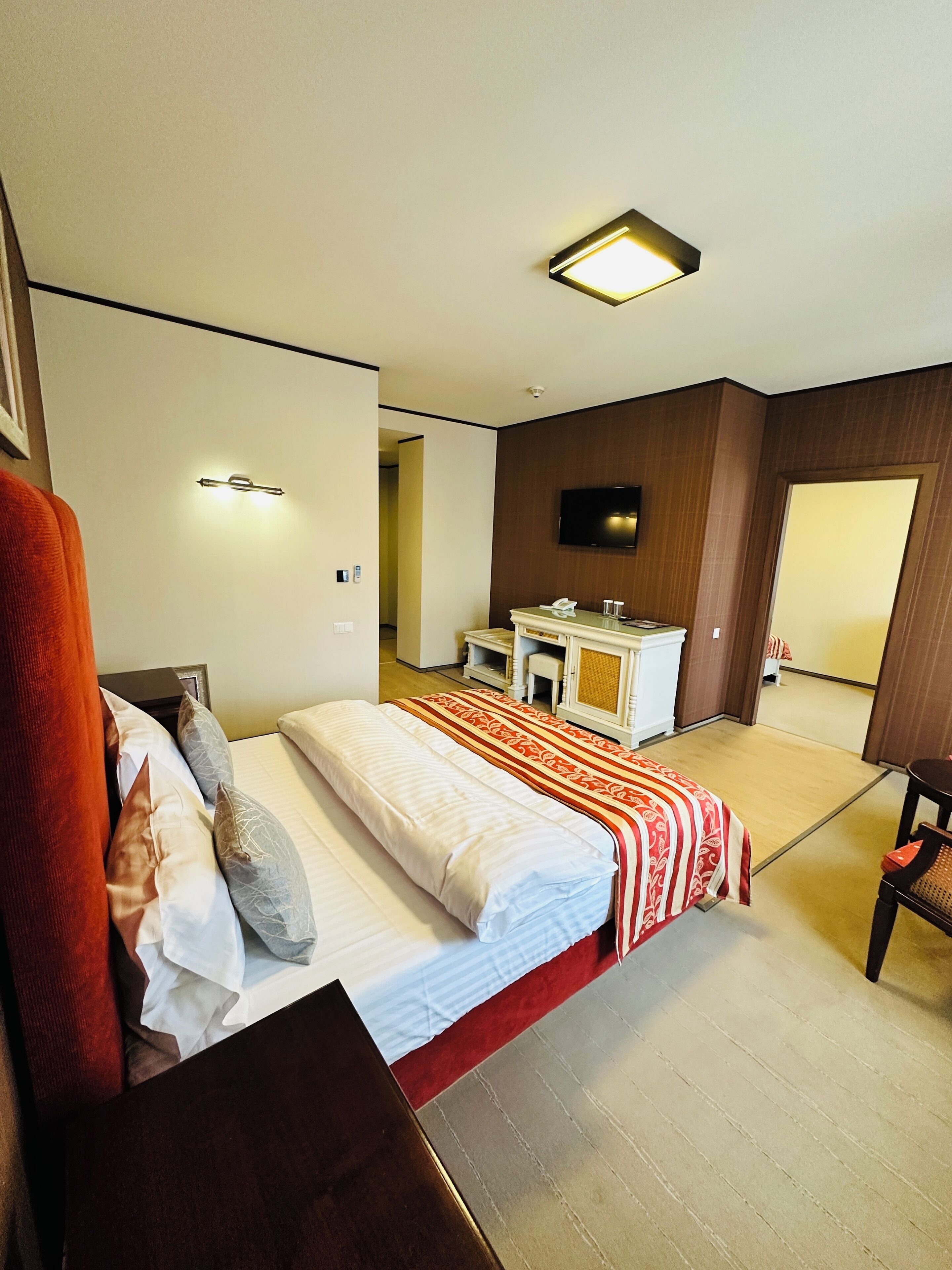 Une chambre d’hôtel équipée d’un lit, d’une table de chevet, d’un miroir et d’un téléviseur fixé au mur.