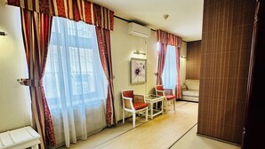 A spacious room with a large window, a small table with chairs, and a wooden floor.