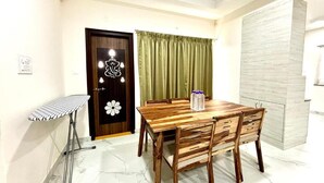 A dining area with a wooden table and chairs, a small folding table, and a door with a decorative emblem. - 3 Bee's Service Apartments (Hyderabad)