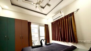 A bedroom with a bed, a ceiling fan, an air conditioning unit, a window with curtains, and a wardrobe. - 3 Bee's Service Apartments (Hyderabad)