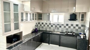 A modern kitchen with dark cabinets, a marble countertop, and a patterned backsplash. - 3 Bee's Service Apartments (Hyderabad)