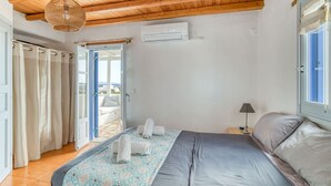 A bedroom with a bed, a nightstand, an air conditioning unit, and a view of the outside balcony. - Quiet area with Beach access (Chrisi Akti)