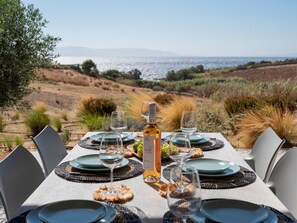 A table set for a meal with a bottle of wine, plates, and glasses, overlooking a natural landscape. - Villa Ena - Beach getaway (Paros)