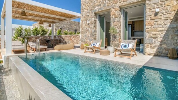 A poolside area with a stone building, lounge chairs, and a pergola. - Spick & span in Paros island (Aspro Chorio)