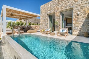 A poolside area with a stone building, lounge chairs, and a pergola.