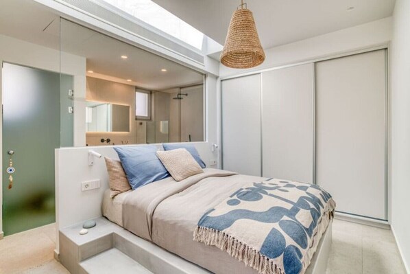 A modern bedroom with a bed, a bedside table, a hanging light fixture, and a wardrobe.