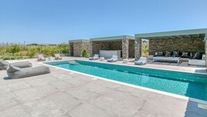 A swimming pool with lounge chairs and a stone wall backdrop.