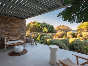 A patio with a stone wall, wicker furniture, and a view of a landscaped garden.