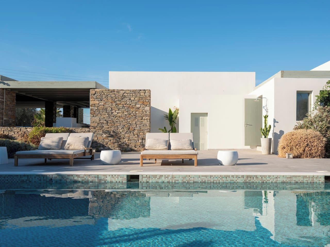 A modern poolside area with a stone wall, a lounge chair, and a potted plant.