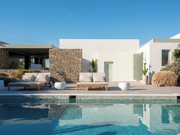 A modern poolside area with a stone wall, a lounge chair, and a potted plant.