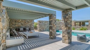 A covered outdoor seating area with stone pillars, a pool, and a stone wall.