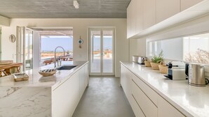A modern kitchen with a view of the beach, a dining area, and a large window.