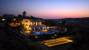 A modern villa with a swimming pool, surrounded by landscaped gardens and a view of the countryside at dusk. - Villa Tchi Tcha - Naoussa Bay (Kamares Naousas)