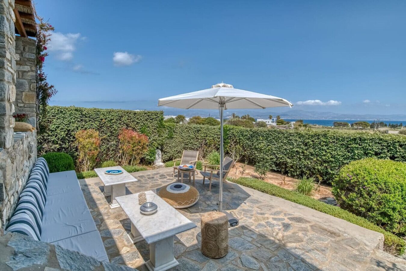 Eine Terrasse mit Steinboden, Gartenmöbeln und einem weißen Sonnenschirm.