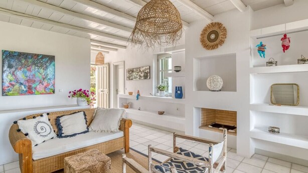 Una sala de estar acogedora con un sofá de mimbre, una lámpara colgante tejida y una chimenea.