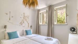 Una habitación de hotel con dos camas, una ventana con cortinas, un ventilador en la pared y una lámpara en la mesita de noche.