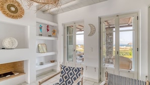 Una habitación luminosa y espaciosa con chimenea, una silla con estampado y vista al mar a través de una puerta.