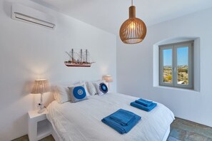 A bedroom with a bed, two bedside lamps, a ship decoration, a hanging light fixture, and a window with a view.