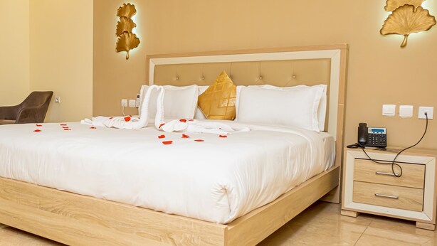 A hotel room with a large bed, a wooden nightstand with a phone, and a chair. - HOTEL GOLDEN PLAZZA CONAKRY (Conakry)