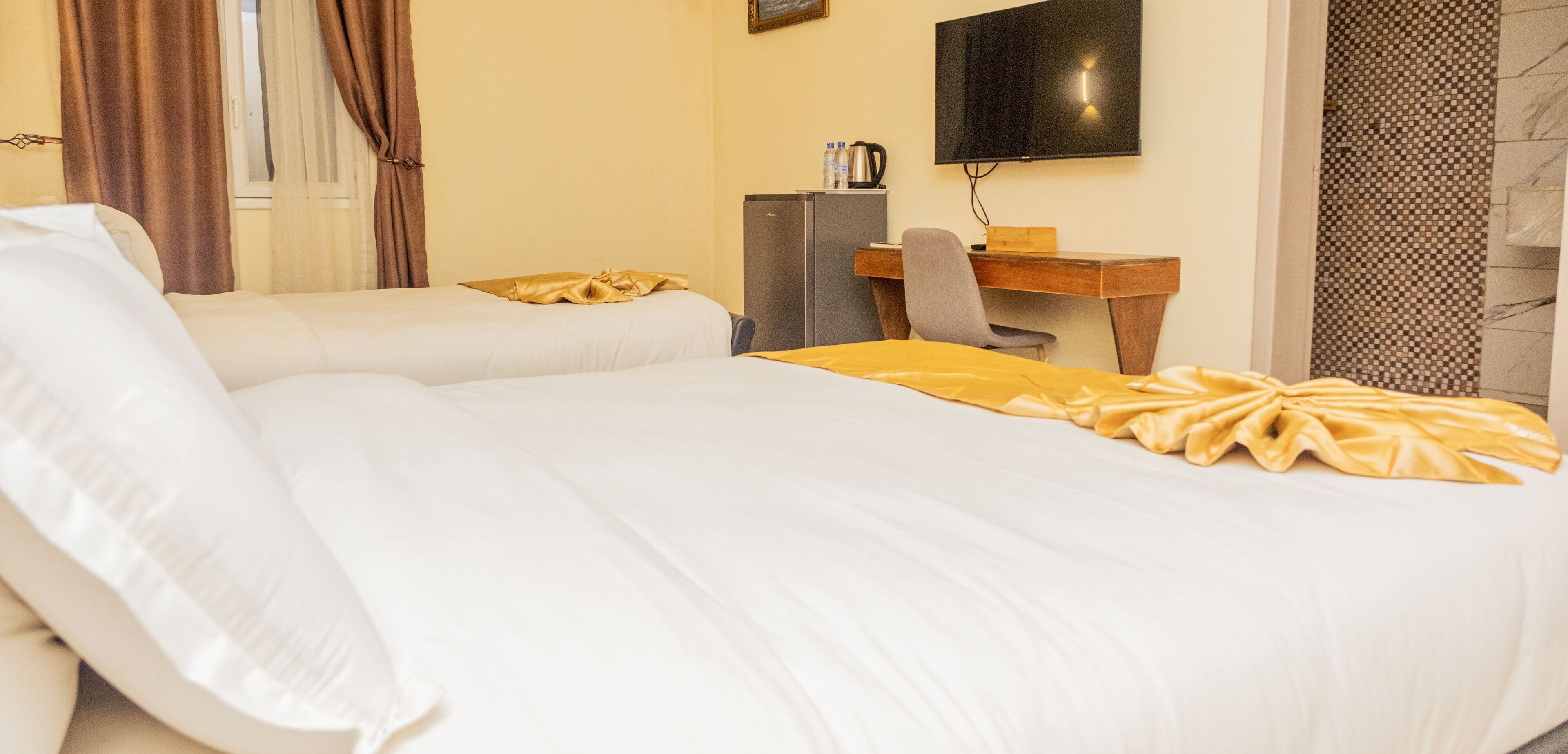Habitación de hotel con dos camas, un escritorio, televisión y refrigerador.
