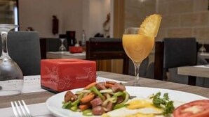 A dining table with a plate of food, a glass of orange juice, and a red box. - HOTEL GOLDEN PLAZZA CONAKRY (Conakry)