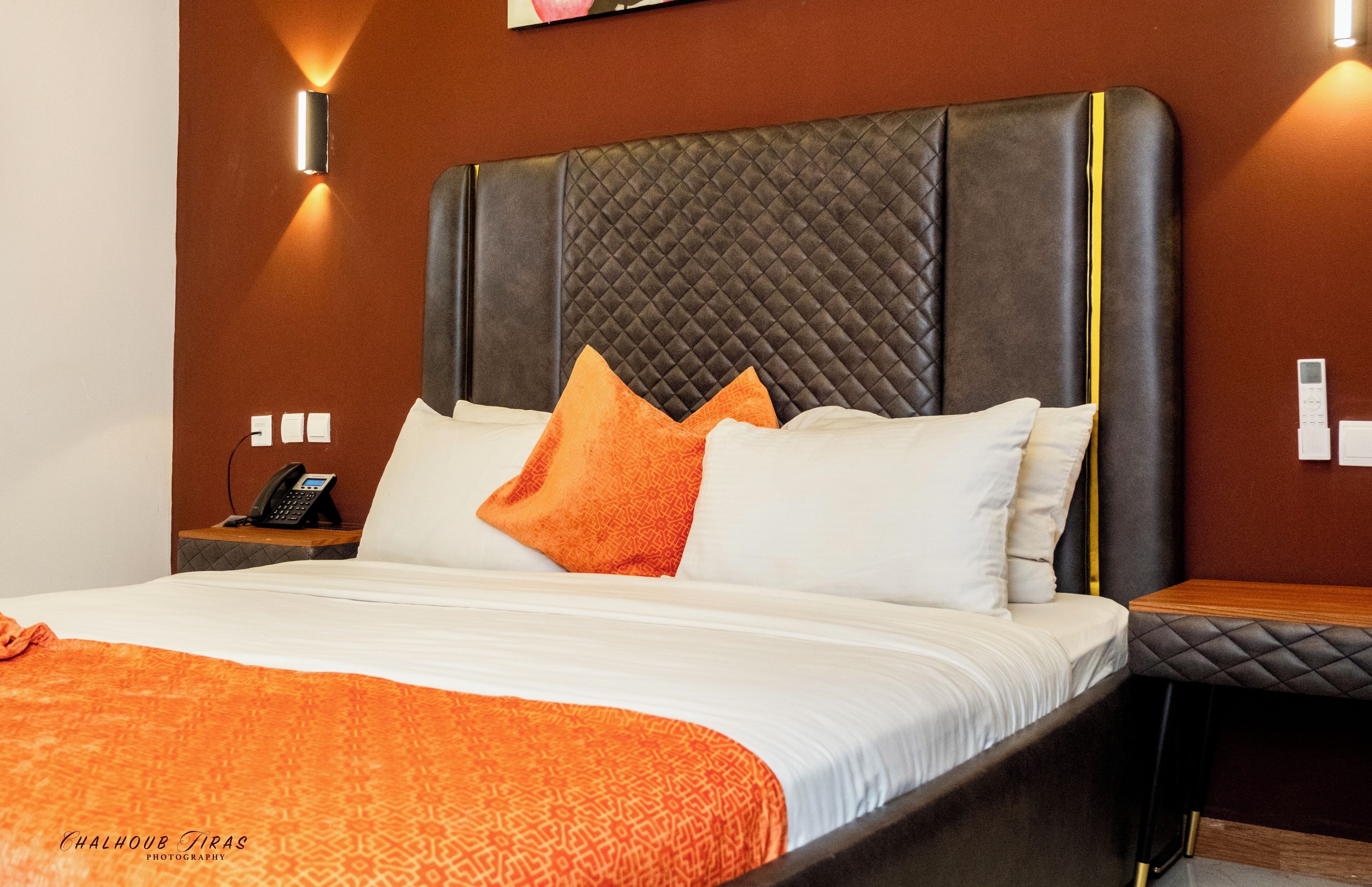 A hotel room with a large bed, a bedside table with a phone, and a wall-mounted light fixture.