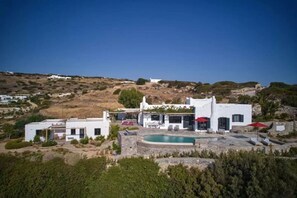 Une villa blanche avec une piscine, entourée de verdure et de collines.