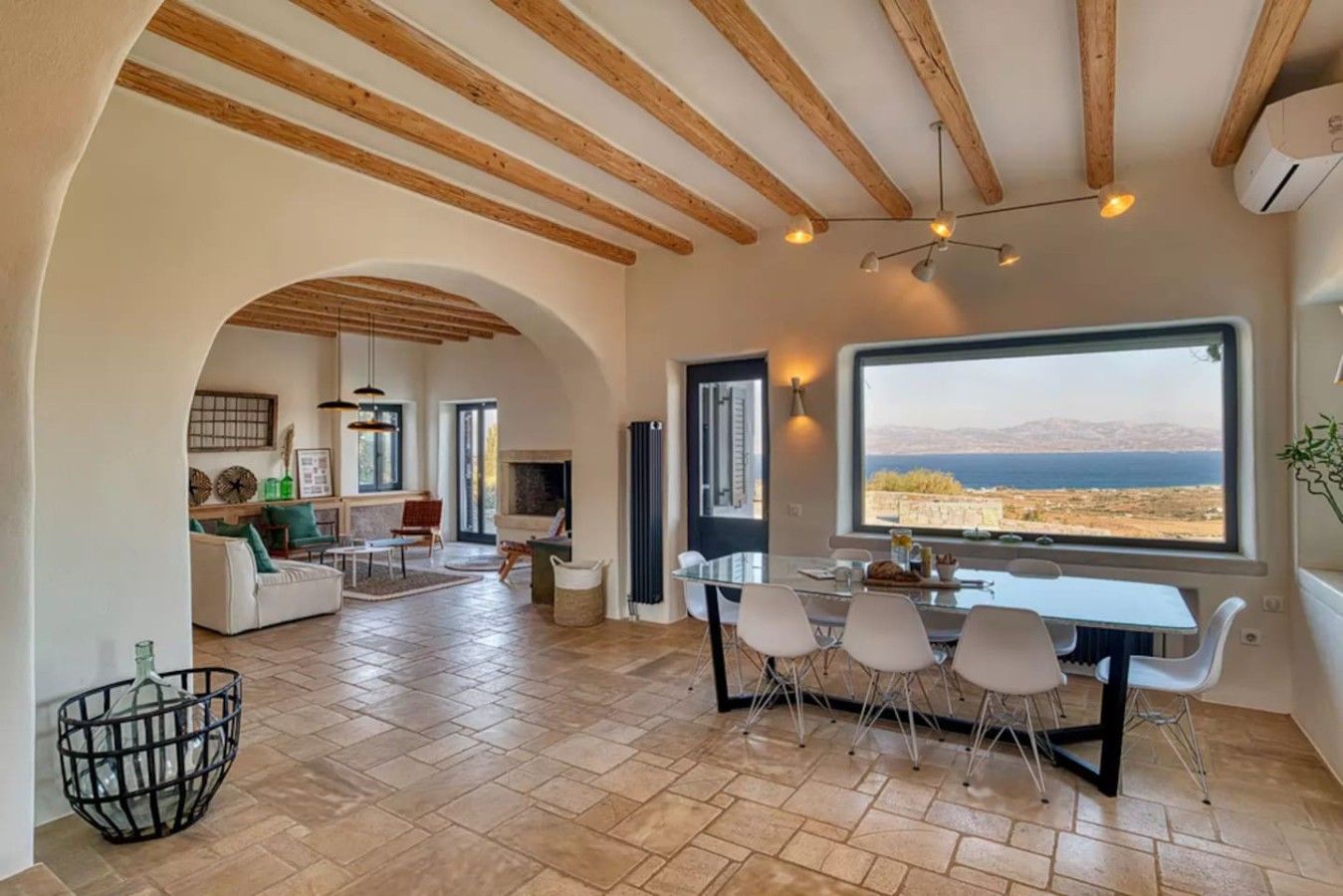 Un vaste espace de vie doté d’une grande fenêtre offrant une vue sur la mer, un coin repas avec une table et des chaises, et un coin salon confortable avec une cheminée.