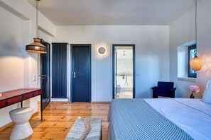 Une chambre moderne avec un grand lit, un bureau, une chaise et une salle de bain visible à travers une porte ouverte.
