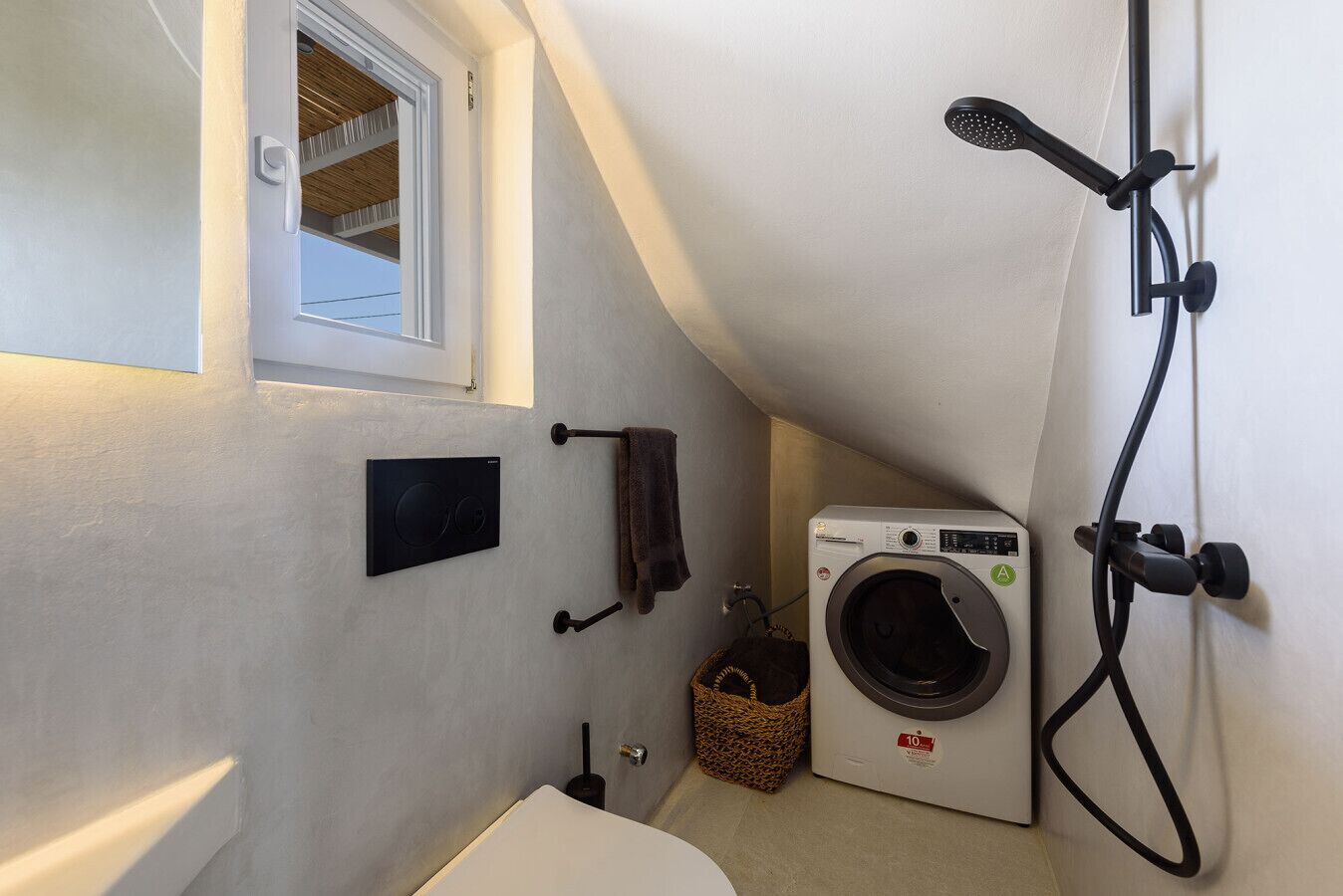 Ein kleines Badezimmer mit integrierter Waschmaschine, Handtuchhalter und Duschkopf.