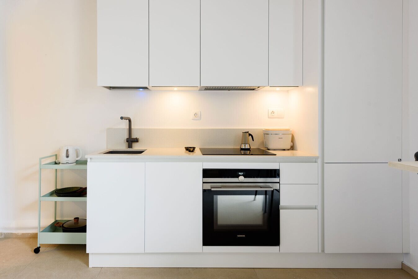 Una cocina moderna con armarios blancos, horno empotrado y una cafetera sobre una estante.