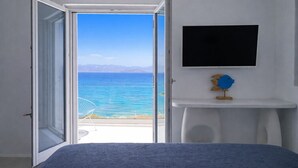 A room with a bed, a TV mounted on a white wall, and a view of the sea through an open door. - Black Pearl Villa - Sea Front (Ampelas)