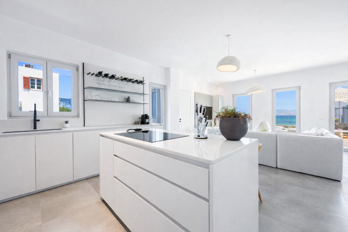 A modern kitchen with a central island, white cabinetry, and a view of the sea through large windows.